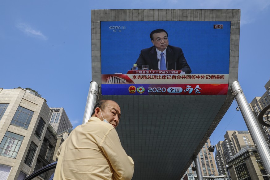 epa08449073 A man stands near a large screen displaying a press conference by Chinese Premier Li Keqiang following the closing ceremony of the third session of the 13th National People&#039;s Congress ...