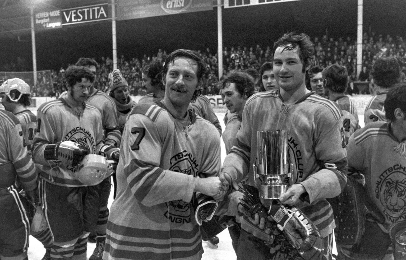 Die Spieler des SC Langnau mit Spielertrainer Jean Cusson, links, und Captain Fritz Lehmann, mit Pokal, feiern am 2. Maerz 1976 in der Ilfishalle in Langnau nach dem Spiel gegen den EHC Biel den Gewin ...