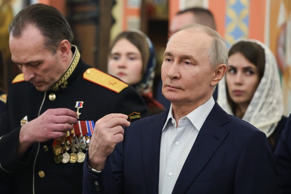 Russian President Vladimir Putin, right, accompanied by military personnel and their families, crosses himself during the Orthodox Christmas service at the Church of Great-Martyr St. George the Victor ...