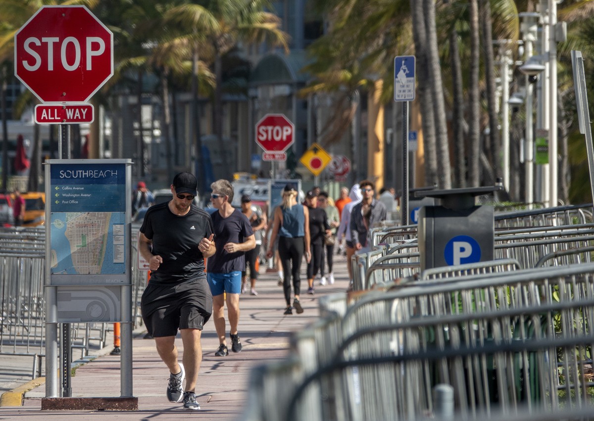 epa08307408 Tourists walk alongside the closed beach in Miami Beach in South Beach, Florida, USA, 19 March 2020. On 15 March, Miami Beach Mayor Dan Gelber implemented new restrictions meant to curb th ...