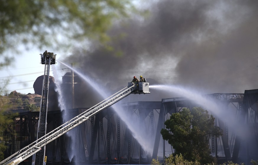 Firefighters try to put out flames from a derailed freight train as it burns on a bridge spanning Tempe Town Lake Wednesday, July 29, 2020, in Tempe, Ariz. Officials say a freight train traveling on t ...
