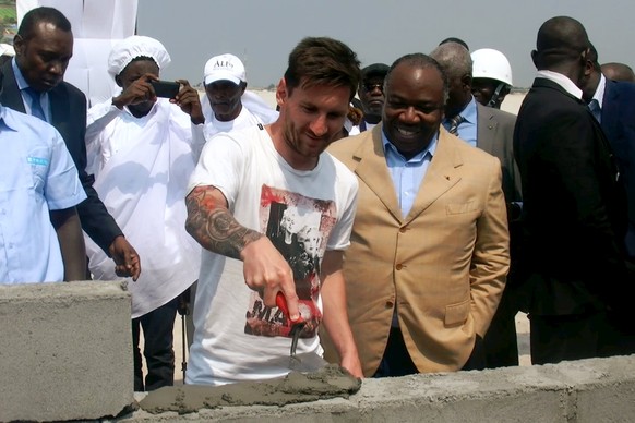 Lionel Messi betätigt sich unter Beobachtung von Gabuns Präsident Ali Bongo (braunes Jacket) als Stadionbauer.