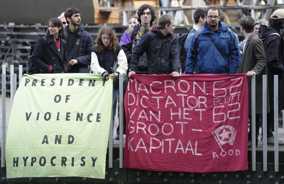 Protesters against pension reforms in France hold a banner "Macron, dictator of big business, who retired at the age of 62, will stay" when French President Emmanuel Macron leaves...