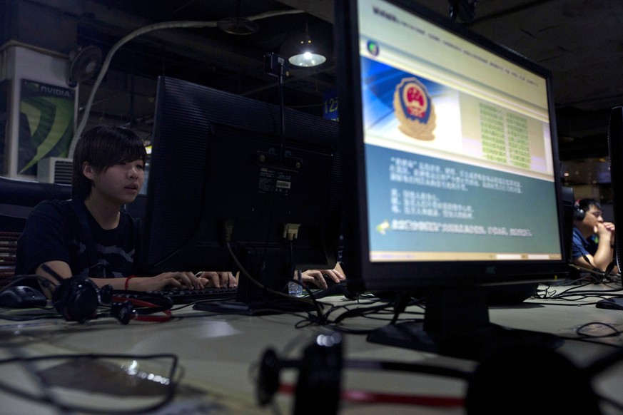 FILE - In this Aug. 19, 2013, file photo, computer users sit near a monitor display with a message from the Chinese police on the proper use of the Internet at an Internet cafe in Beijing. A Chinese o ...