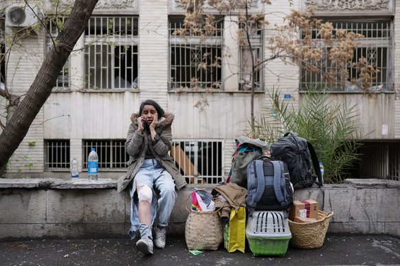 An injured woman talks on her cellphone as she sits next to her belongings after leaving her apartment following a strike that hit a residential building Tehran, Iran, Saturday, March 28, 2026. (AP Ph ...