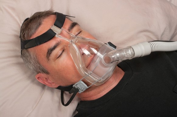 Schlafender Mann mit CPAP-Gerät: Regelmässig angewendet kann die Atemtherapie eine Schlafapnoe und die damit verbundenen Beschwerden deutlich lindern.