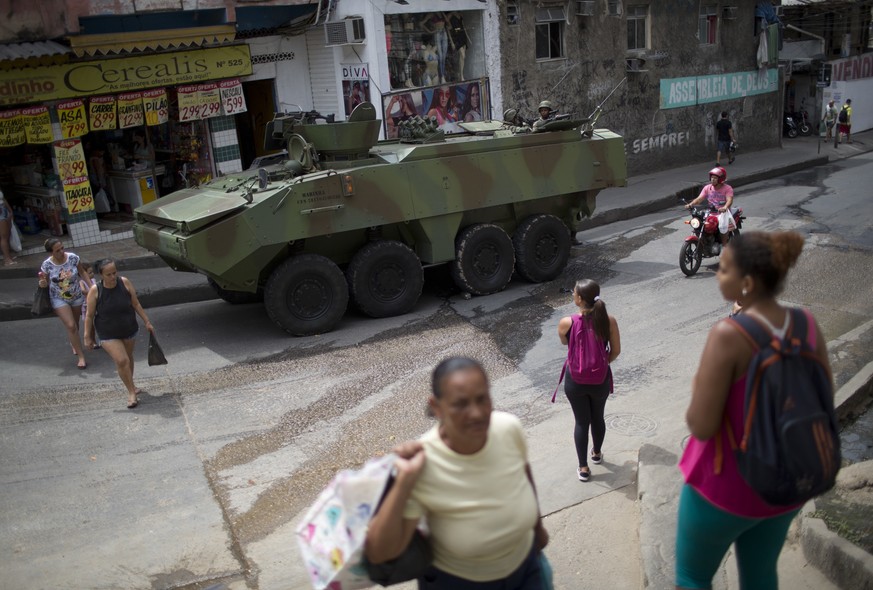 Residents walk past an armored vehicle at the Rocinha favela, in Rio de Janeiro, Brazil, Saturday, Sept. 23, 2017. Shootouts erupted in several areas of Rio de Janeiro on Friday, prompting Brazilian a ...