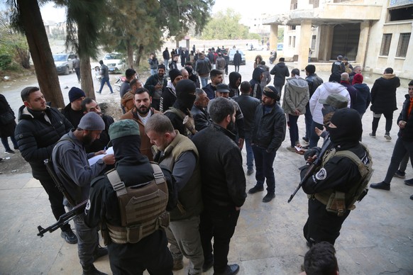 epa11758871 Armed opposition rebels affiliated with the Ministry of Interior of the Syrian Salvation Government secure the area as people wait for the registration for their status after the oppositio ...