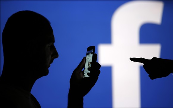 A man is silhouetted against a video screen with a Facebook logo as he poses with a Samsung S4 smartphone in this file photo illustration taken in the central Bosnian town of Zenica August 14, 2013. O ...