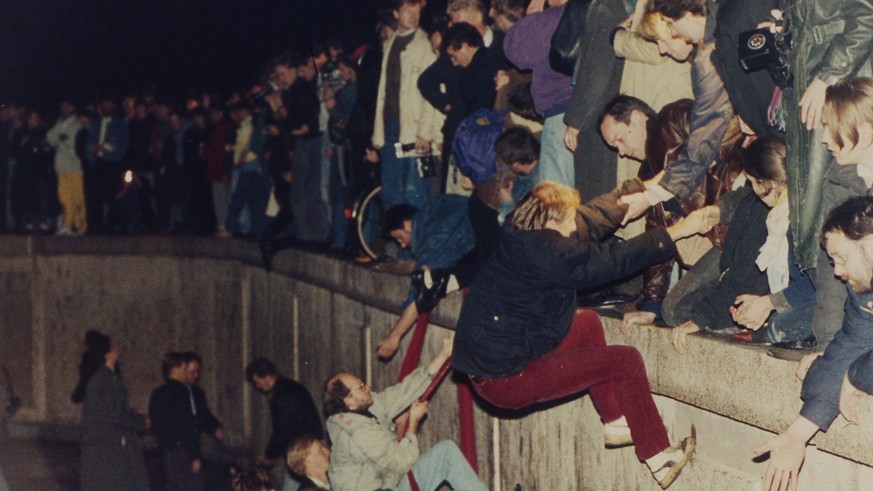 East Berliners get helping hands from West Berliners as they climb the Berlin Wall which has divided the city since the end of World War II, near the Brandenburger Tor (Brandenburg Gate), early mornin ...