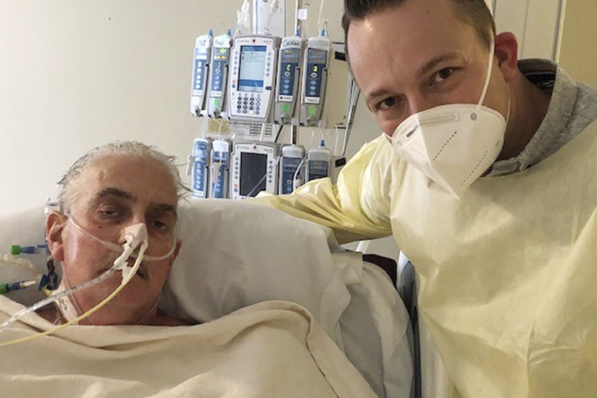 In this photo provided by the University of Maryland School of Medicine, David Bennett Jr., right, stands next to his father's hospital bed in Baltimore, Md., on Jan. 12, 2022, five days after do ...