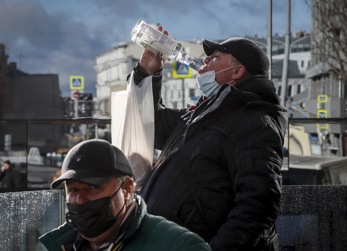 epa09572387 A Russian man in protective face mask drinks vodka from the bottle on the street in front of a mirror window amid the ongoing coronavirus COVID-19 pandemic in Moscow, Russia, 09 November 2 ...