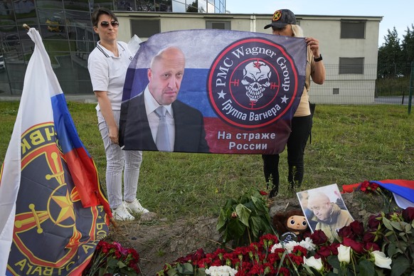 Women hold a flag with an image of the owner of private military company Wagner Group Yevgeny Prigozhin at an informal memorial next to the former &#039;PMC Wagner Centre&#039; in St. Petersburg, Russ ...