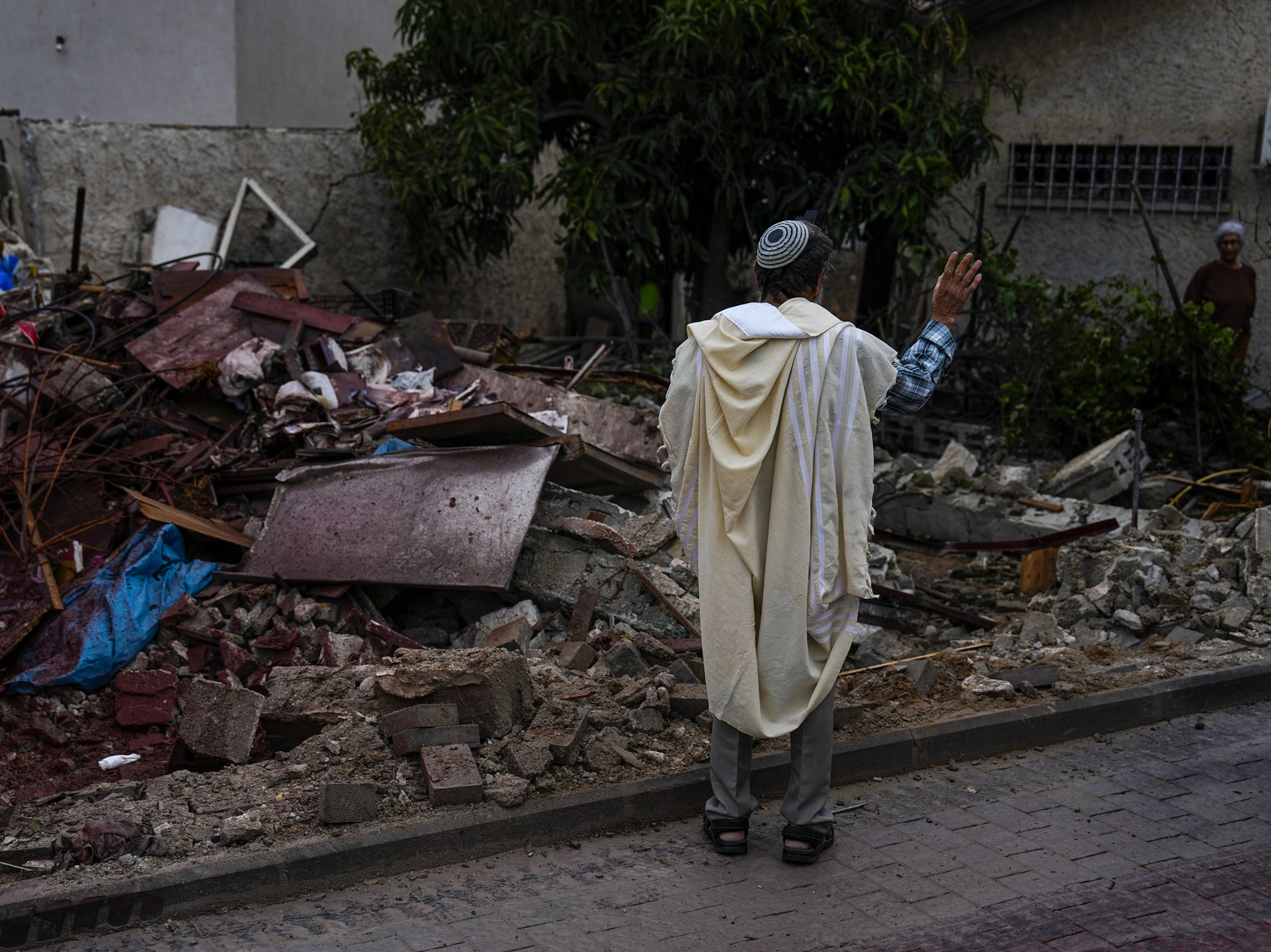 A man wrapped in a prayer shawl holds a holy book as he stands near a building destroyed by a rocket fired from the Gaza Strip by Palestinian militants, in Ashkelon, Israel, Thursday, March.