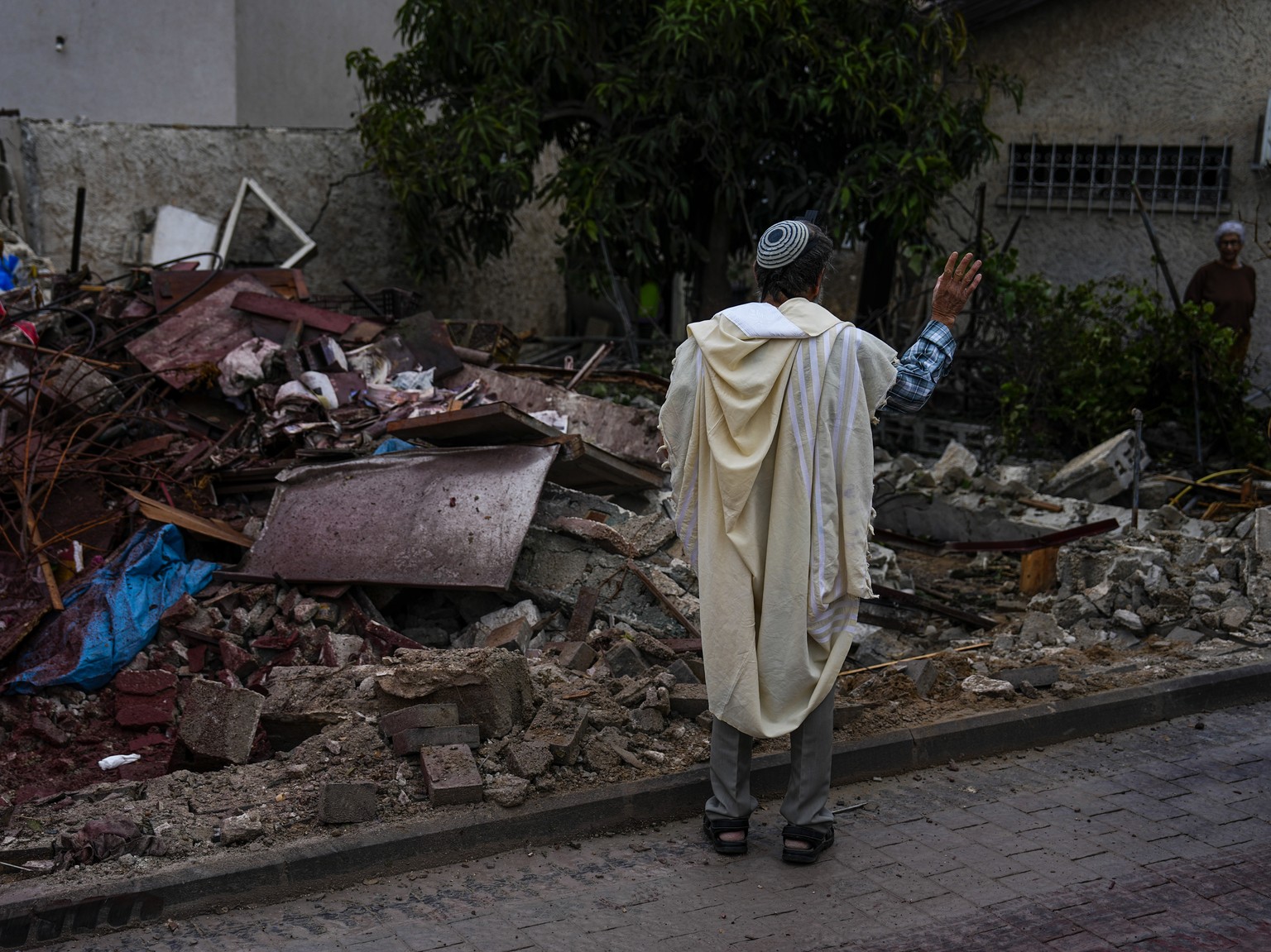 A man covered in a prayer shawl holds a holy book as he stands by a structure destroyed by a rocket fired Wednesday night from the Gaza Strip by Palestinian militants, in Ashkelon, Israel, Thursday, M ...