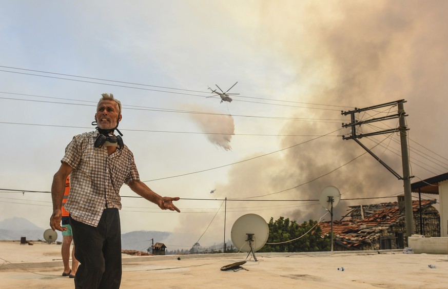 A man reacts as a helicopter pours water over the fire-devastating Sirtkoy village, near Manavgat, Antalya, Turkey, Sunday, Aug. 1, 2021. More than 100 wildfires have been brought under control in Tur ...