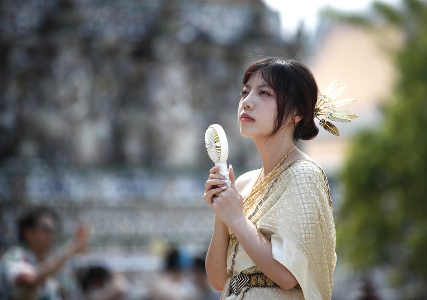 epa11321382 A Chinese tourist uses a handheld electric fan to cool from the heat amid hot weather at the Temple of Dawn, or Wat Arun, in Bangkok, Thailand, 06 May 2024. Thailand is facing a severe hea ...