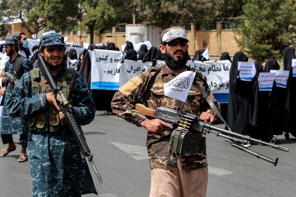 epa09461007 Taliban forces stand guard at a roadside Afghan women hold placards during a pro-Taliban rally outside the Shaheed Rabbani Education University in Kabul, Afghanistan, 11 September 2021. Th ...