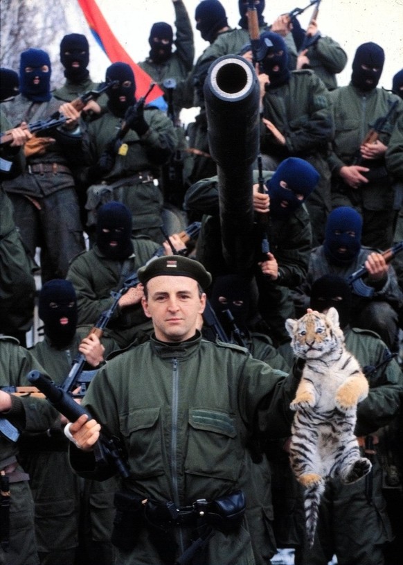 1991 photo showing Serbian warlord Zeljko Raznatovic, better known as &quot;Arkan&quot; holding a tiger cub, symbol of his unit called &quot;Tigers&quot;, posing with his masked soldiers in front of t ...