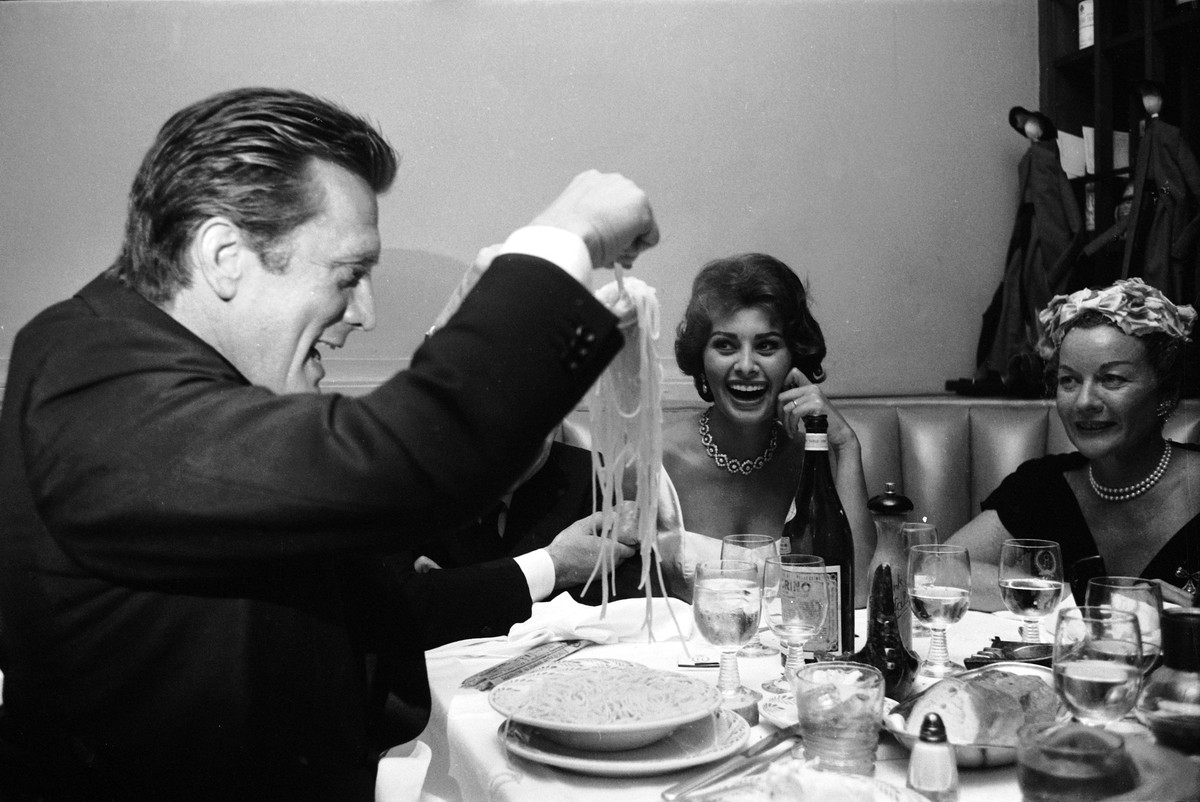 American actor Kirk Douglas serves himself a mound of spaghetti as Italian film producer Carlo Ponti (obscured), his wife, Italian actor Sophia Loren, and an unidentified woman in a pearl necklace wat ...