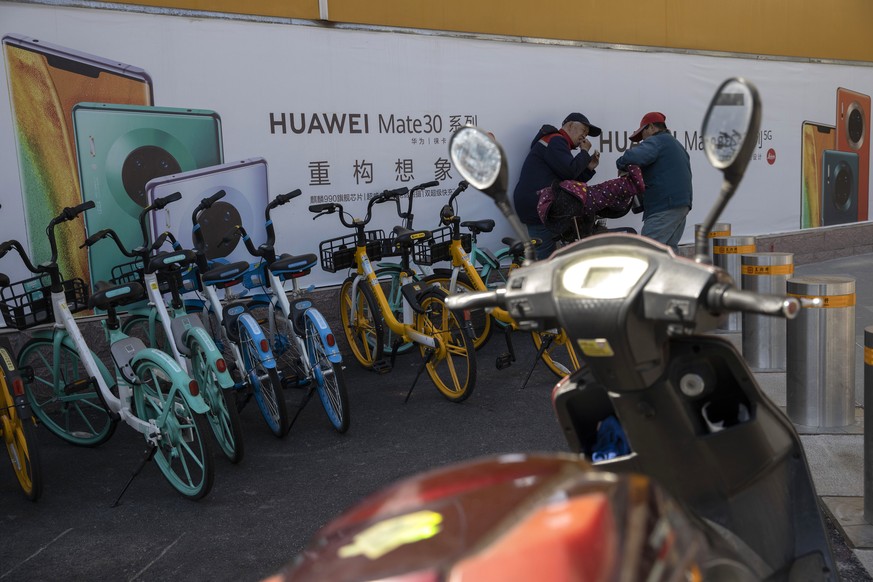 In this photo taken Sunday, March 22, 2020, men chat near advertisements for Huawei mobile phones in Beijing. Chinese tech giant Huawei says Tuesday, March 31, 2020, its 2019 sales rose 19.1% over a y ...