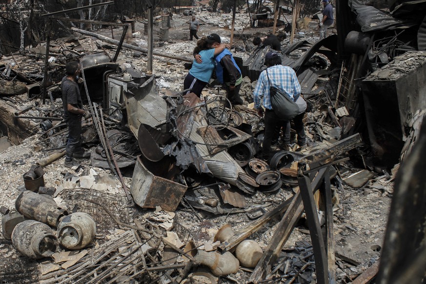 Local residents hug each other amid rubble and burned-out homes after wildfires reached their neighborhood in Vina del Mar, Chile, Sunday, Feb. 4, 2024.  (AP Photo/Cristobal Basaure)
