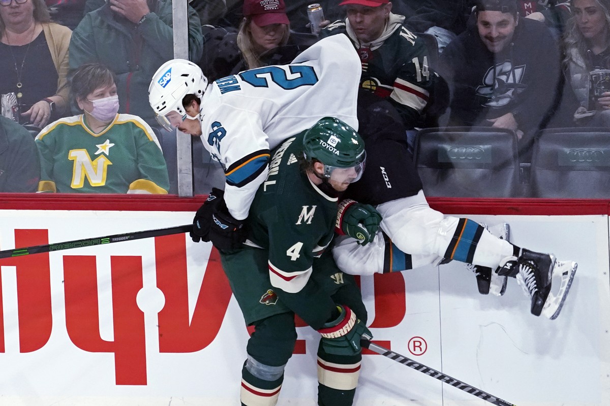 San Jose Sharks' Jasper Weatherby (26) takes a mid-air check from Minnesota Wild's Jon Merrill (4) during the first period of an NHL hockey game Tuesday, Nov. 16, 2021, in St. Paul, Minn. (A ...