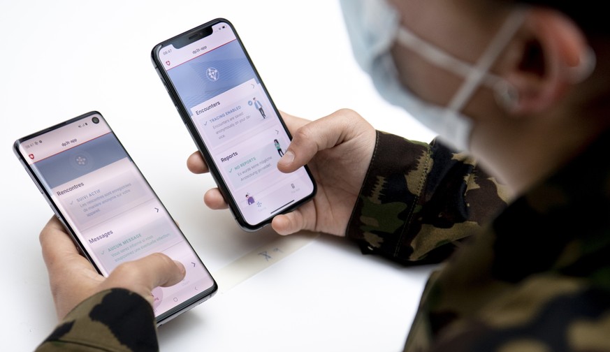 Soldier of the Swiss army wearing protective face mask looking at Android and iOS (Google and Apple) smartphone during a test of a smart phone app using Decentralized Privacy-Preserving Proximity Trac ...