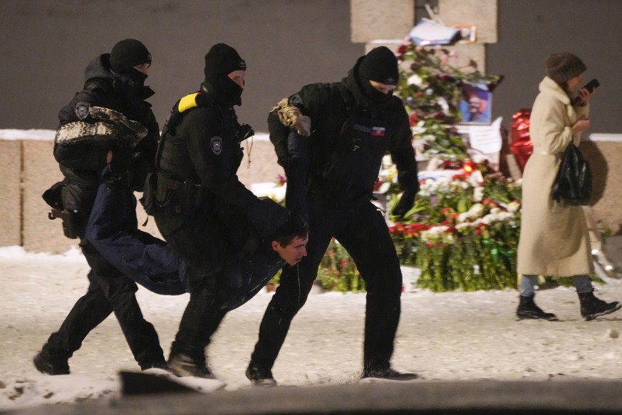 FILE - Police detain a man laying flowers in tribute to the late Alexei Navalny at the Memorial to Victims of Political Repression in St. Petersburg, Russia, on Friday, Feb. 16, 2024. Navalny, the fie ...