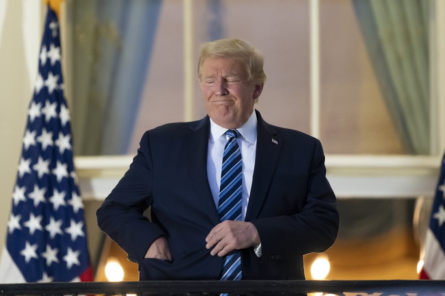 President Donald Trump puts his mask in his pocket as he stands on the Blue Room Balcony upon returning to the White House Monday, Oct. 5, 2020, in Washington, after leaving Walter Reed National Milit ...