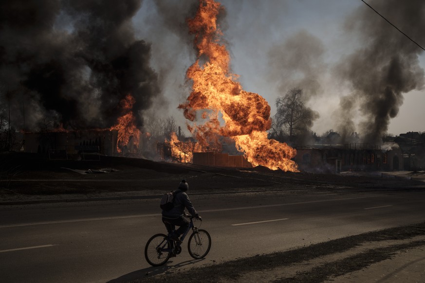 FILE - A man rides his bike past flames and smoke rising from a fire following a Russian attack in Kharkiv, Ukraine, on March 25, 2022. With its aspirations for a quick victory dashed by a stiff Ukrai ...