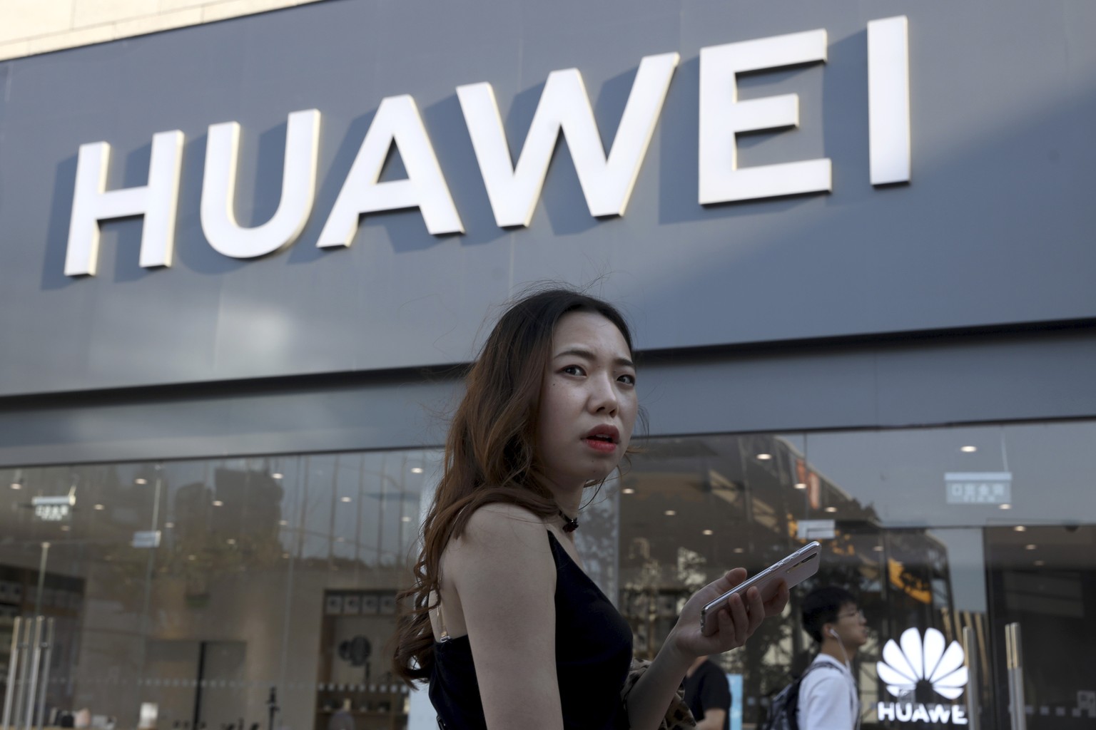 A woman uses a smartphone outside a Huawei store in Beijing Monday, May 20, 2019. Google is assuring users of Huawei smartphones the American company's services still will work on them following U.S.  ...