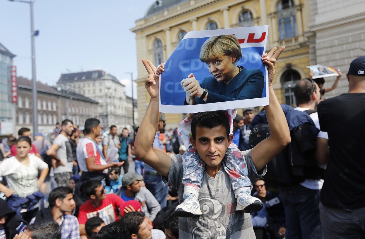 FILE - A migrant holds up a poster of German Chancellor Angela Merkel before starting a march out of Budapest, Hungary, towards Austria and Germany, Sept. 4, 2015. Merkel became the face of a welcomin ...
