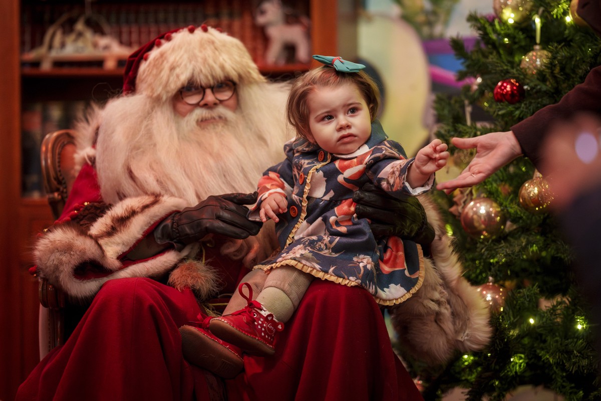 Diana, 22 months old, reaches for her mother's hand as she poses with a man wearing a Santa Claus outfit at Christmas fair in Bucharest, Romania, Saturday, Dec. 14, 2024. (AP Photo/Vadim Ghirda)