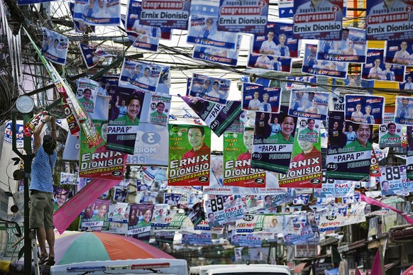A man hangs election campaign posters near a polling center in Manila, Philippines on Friday, May 6, 2022. The son of the late dictator Ferdinand Marcos Sr., Ferdinand Marcos Jr. and the current Vice- ...