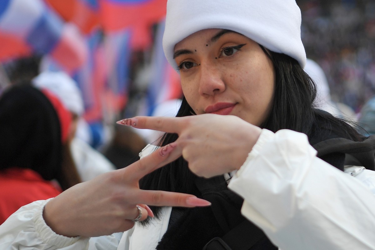 A young woman shows the letter Z, which has become a symbol of the Russian military, and a hashtag reading "We don't abandon our own" as other people with Russian national flags gather  ...