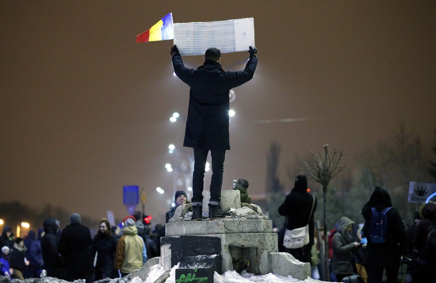 epa05760302 A young man standing on a postament, waves a placard and a small Romanian flag during a protest rally in front of government headquarters in Bucharest, Romania, 29 January 2017. Up to 25,0 ...