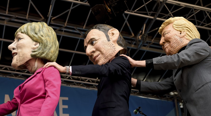 Demonstrators against the G20 Summit stand on stage wearing masks depicting German Chancellor Angela Merkel, left, French President Emmanuel Macron, center, and US President Donald Trump in Hamburg, G ...
