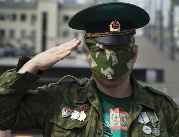 A former Russian border guard wearing a face mask to protect against coronavirus salutes as he gathers with his comrades to celebrate border guards day in front of the closed Gorky Park in Moscow, Rus ...
