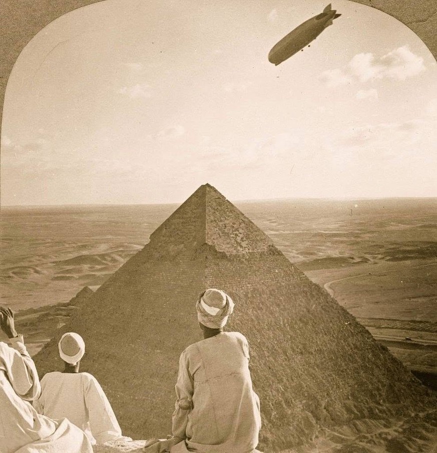Egyptian men watch as the Graf Zeppelin floats over the Great Pyramids of Giza, Egypt, while sitting atop the Great Pyramid, 1931.
