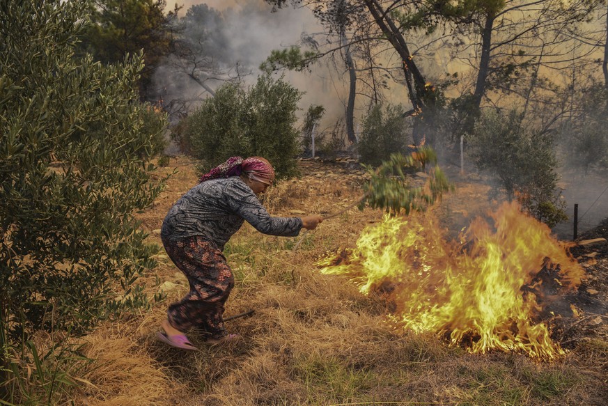A woman tries to stop an advancing wildfire in Kacarlar village near the Mediterranean coastal town of Manavgat, Antalya, Turkey, Saturday, July 31, 2021. The death toll from wildfires raging in Turke ...