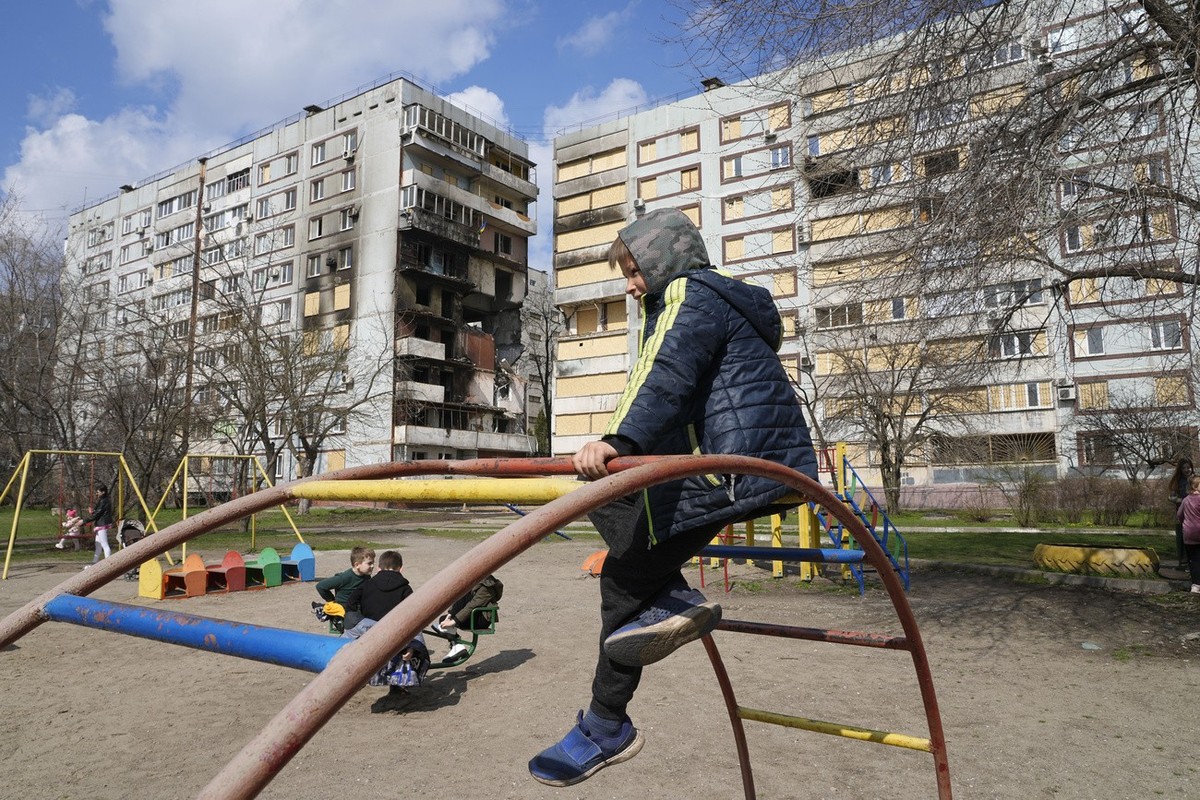 Children play in a playground in front of missile-damaged buildings ahead of a visit by Ukraine's President Volodymyr Zelenskyy Zaporizhzhia, Ukraine, Monday March 27, 2023. (AP Photo/Efrem Lukat ...