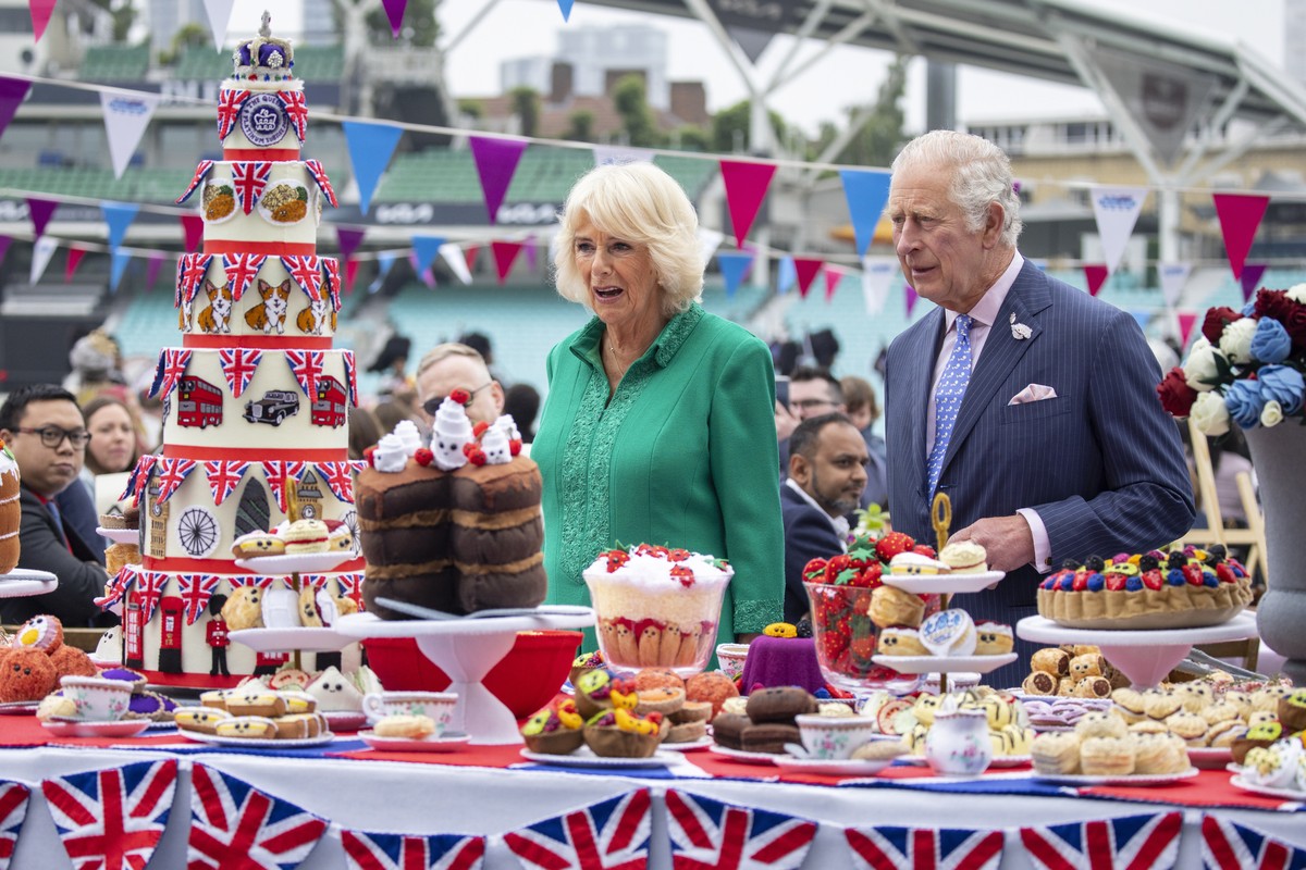 epa09997061 Britain's Prince Charles, the Prince of Wales (R) and Camilla Duchess of Cornwall (L) look at hand-sewn street party decorations as they attend The Big Lunch at the Oval Kennington to ...