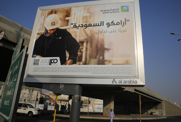 FILE - A man walks under a billboard displaying an advertisement for Saudi Arabia&#039;s state-owned oil giant Aramco with Arabic reading &quot;Saudi Aramco, soon on stock exchange&quot; in Jiddah, Sa ...
