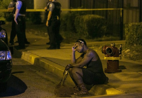 In this Aug. 7, 2016, photo, a woman sits on the curb as police in the background investigate the scene where gunfire at a birthday party left a man dead and a woman injured. The city&#039;s police de ...