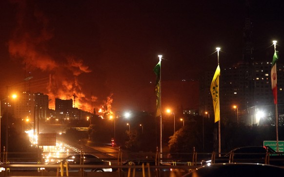 epa12176393 People drive as fire and smoke rise from an oil warehouse in Tehran, Iran, 15 June 2024. Israel continues strikes on Iran?s nuclear program and energy facilities. EPA/ABEDIN TAHERKENAREH