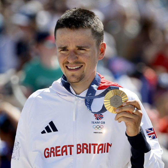 epa11505987 Thomas Pidcock of Great Britain poses with his gold medal after winning the Men Cross Country race of the Mountain Biking competitions in the Paris 2024 Olympic Games, at the Elancourt Hil ...