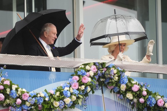Britain's King Charles III and Queen Camilla wave to the crowd from the royal box during Derby Day of the Betfred Derby Festival at Epsom Downs Racecourse, England, Saturday June 6, 2026. (Jonath ...
