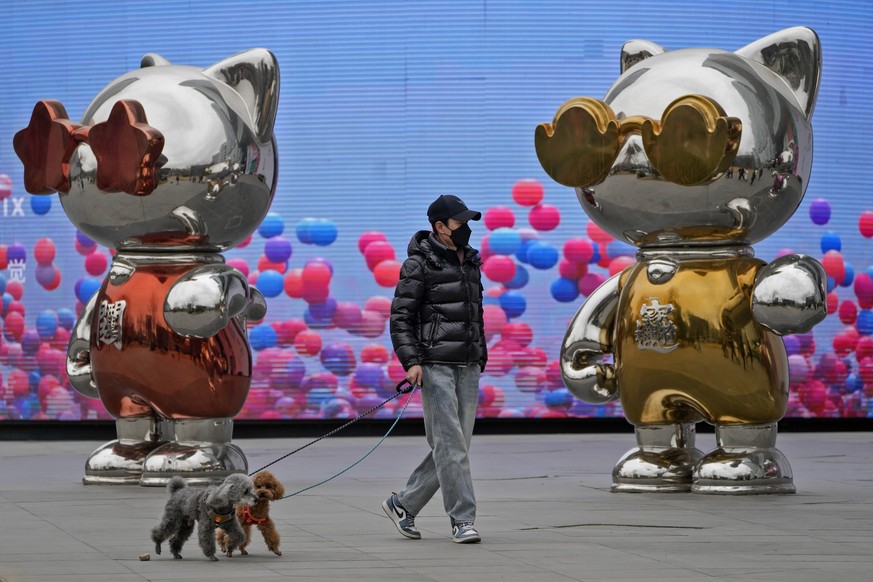 A man walk dogs past cat statues outside a shopping and office complex in Beijing, Saturday, March 11, 2023. China on Saturday named Li Qiang, a close confidant of top leader Xi Jinping, as the countr ...
