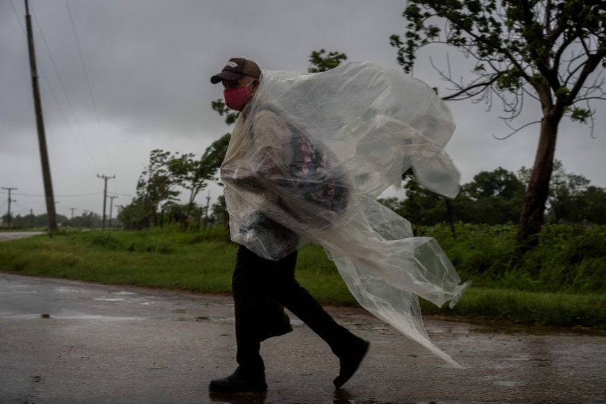 A man, using pieces of plastic against the rain caused by Hurricane Ida, walks on a road leading to Batabano, in the Mayabeque province, Cuba, Friday, Aug. 27, 2021. (AP Photo/Ramon Espinosa)